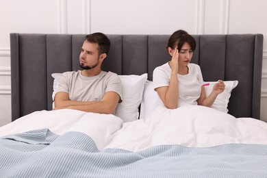 Photo of Worried young couple with pregnancy test on bed at home