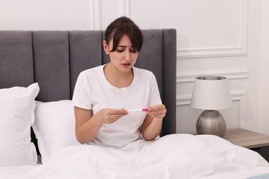 Photo of Worried young woman with pregnancy test on bed at home