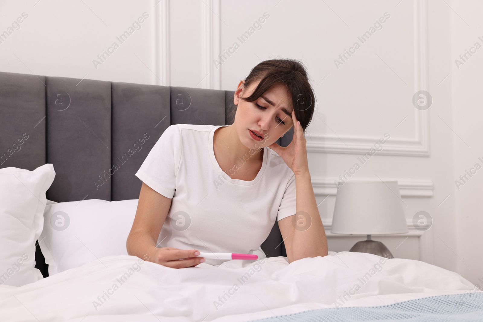 Photo of Worried young woman with pregnancy test on bed at home