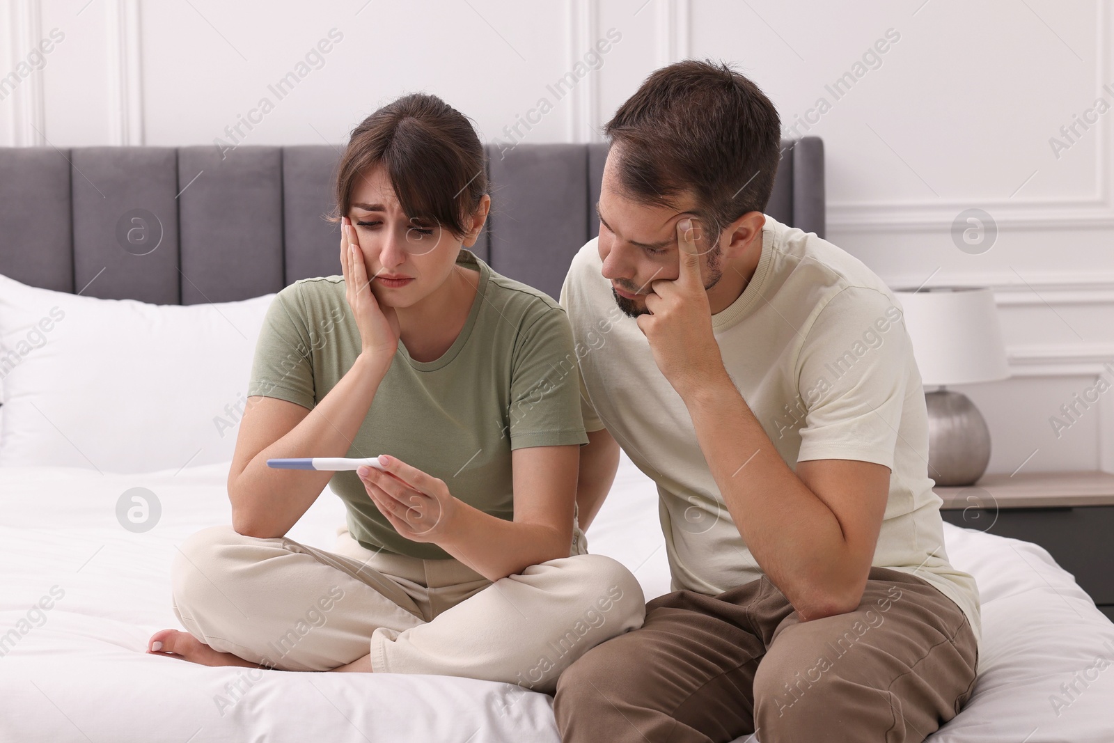 Photo of Worried young couple with pregnancy test on bed at home