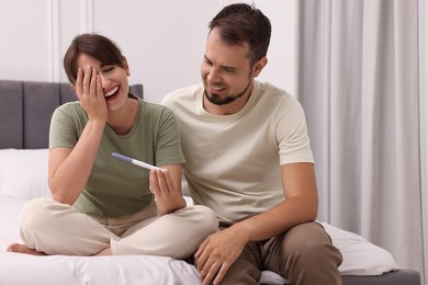 Happy young couple with pregnancy test on bed at home