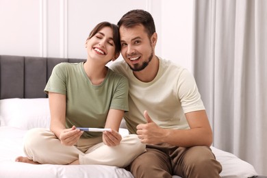 Photo of Happy young couple with pregnancy test on bed at home