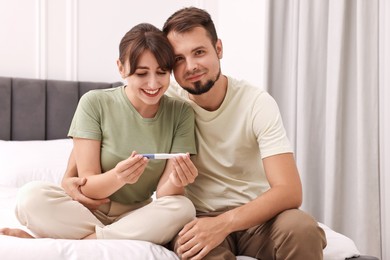 Photo of Happy young couple with pregnancy test on bed at home