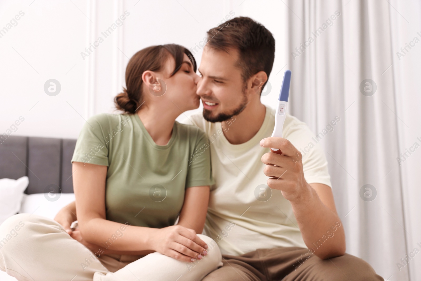 Photo of Happy young couple with pregnancy test at home, selective focus