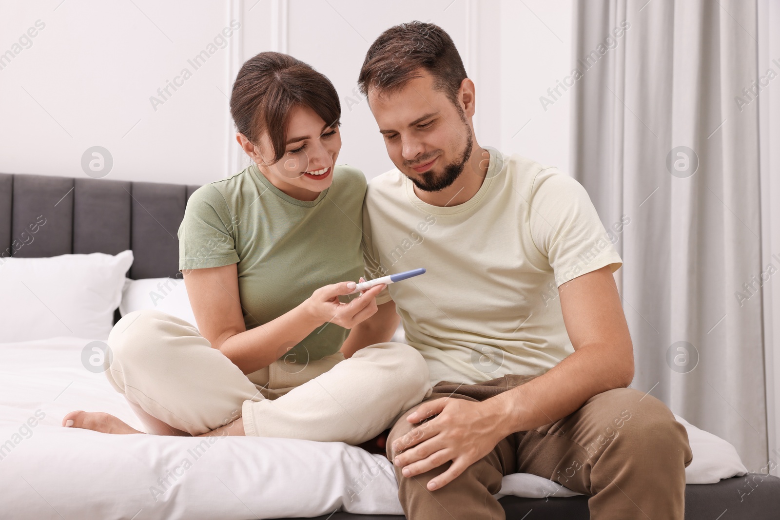 Photo of Happy young couple with pregnancy test on bed at home