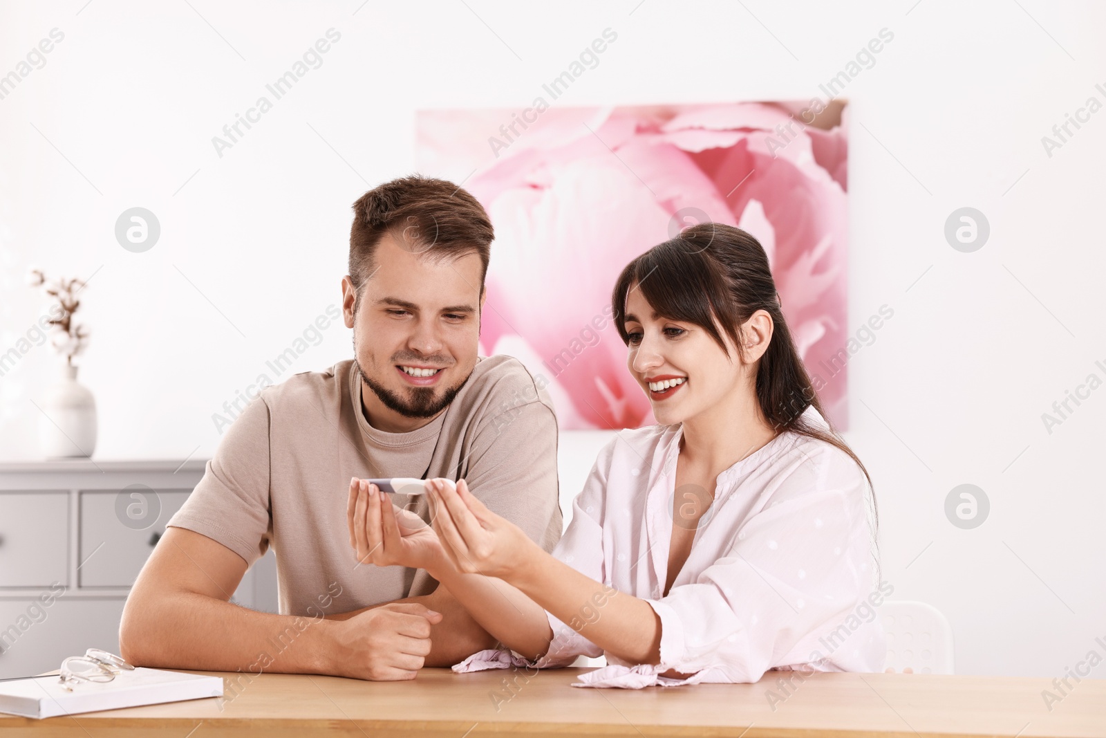 Photo of Happy young couple with pregnancy test at wooden table indoors