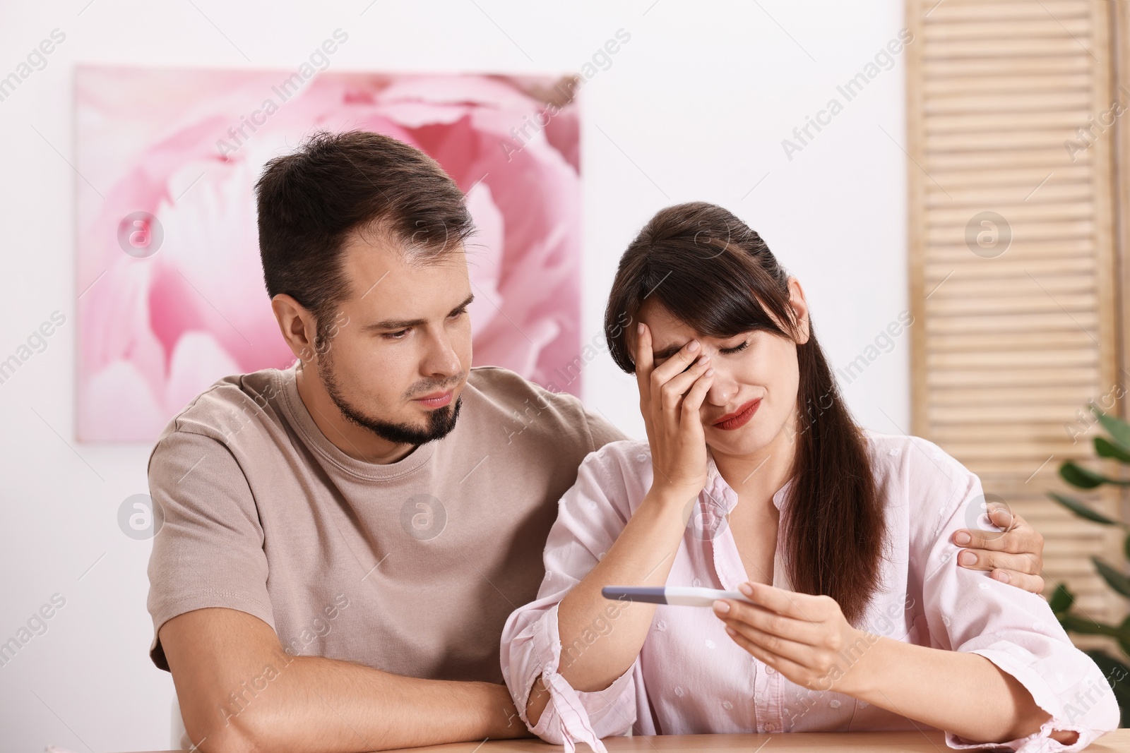 Photo of Worried young couple with pregnancy test at wooden table indoors