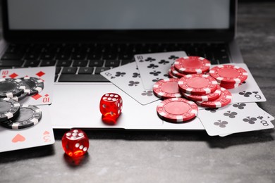 Photo of Poker chips, laptop, playing cards and dices on grey textured table. Online game