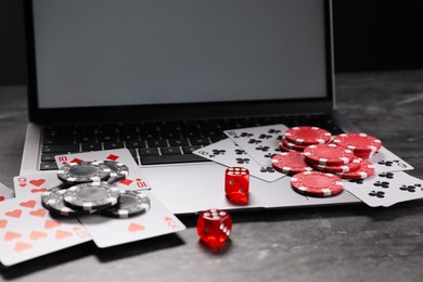 Photo of Poker chips, laptop, playing cards and dices on grey textured table. Online game