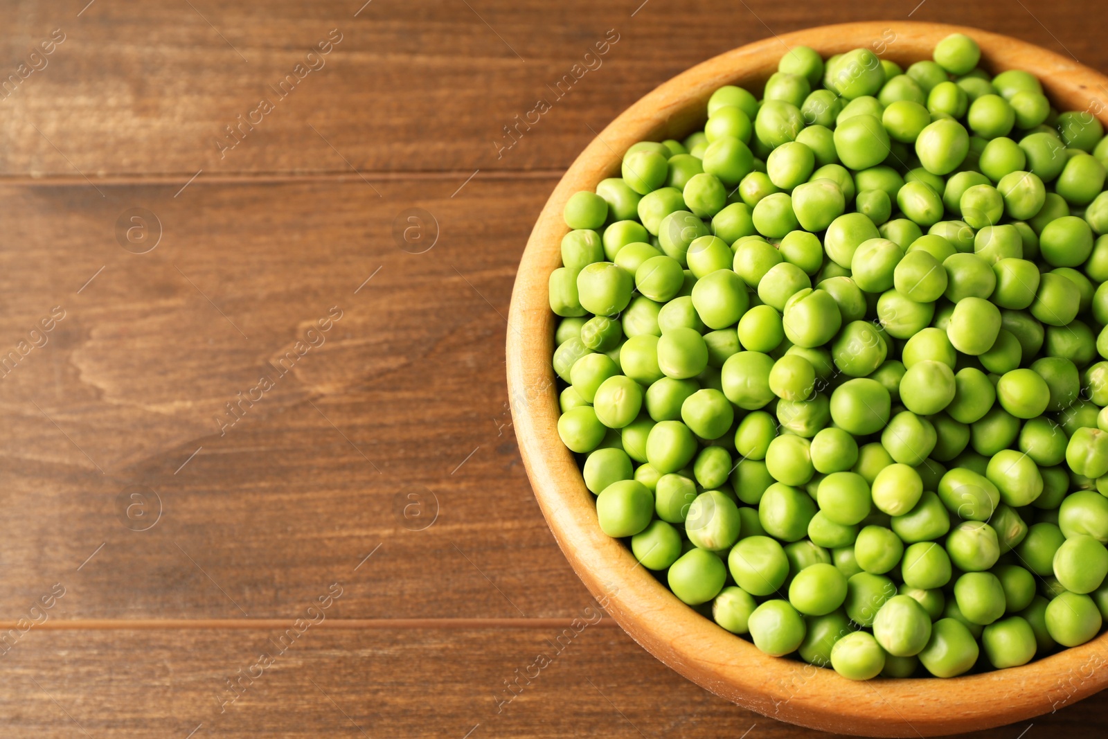 Photo of Fresh green peas in bowl on wooden table. Space for text