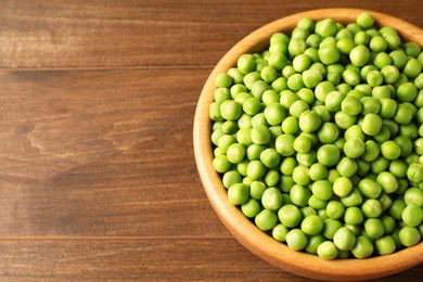 Photo of Fresh green peas in bowl on wooden table. Space for text