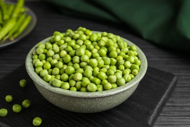 Photo of Fresh green peas in bowl on black wooden table, closeup