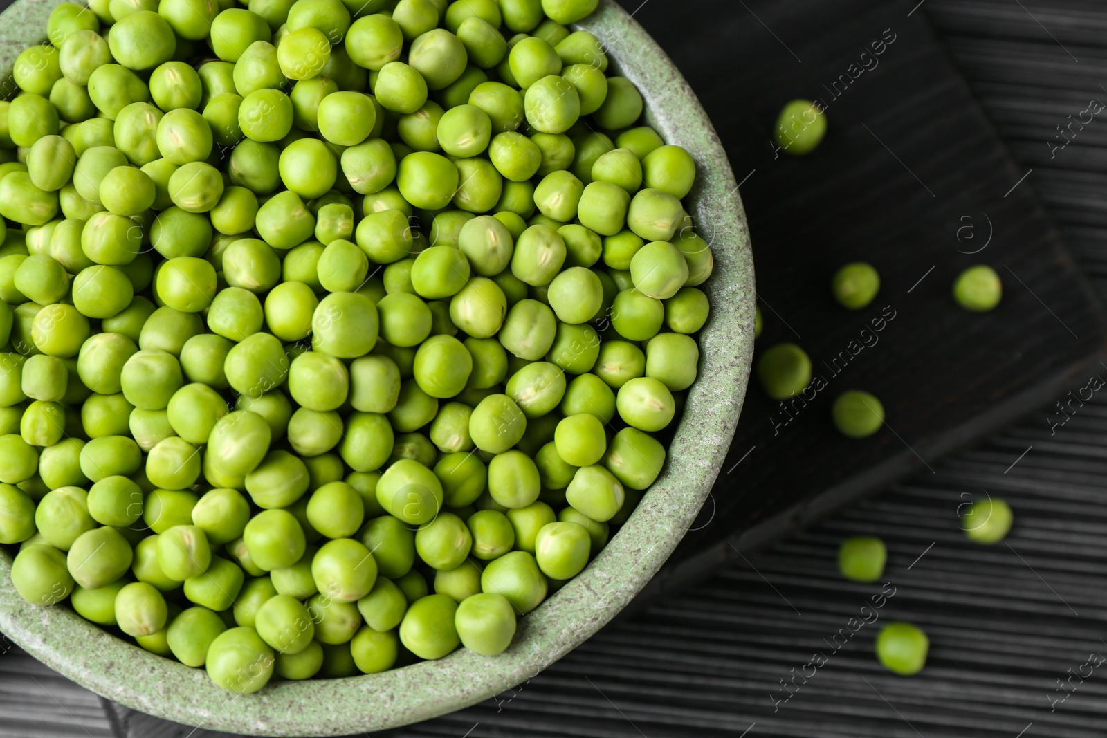 Photo of Fresh green peas in bowl on black wooden table, top view