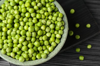 Photo of Fresh green peas in bowl on black wooden table, top view