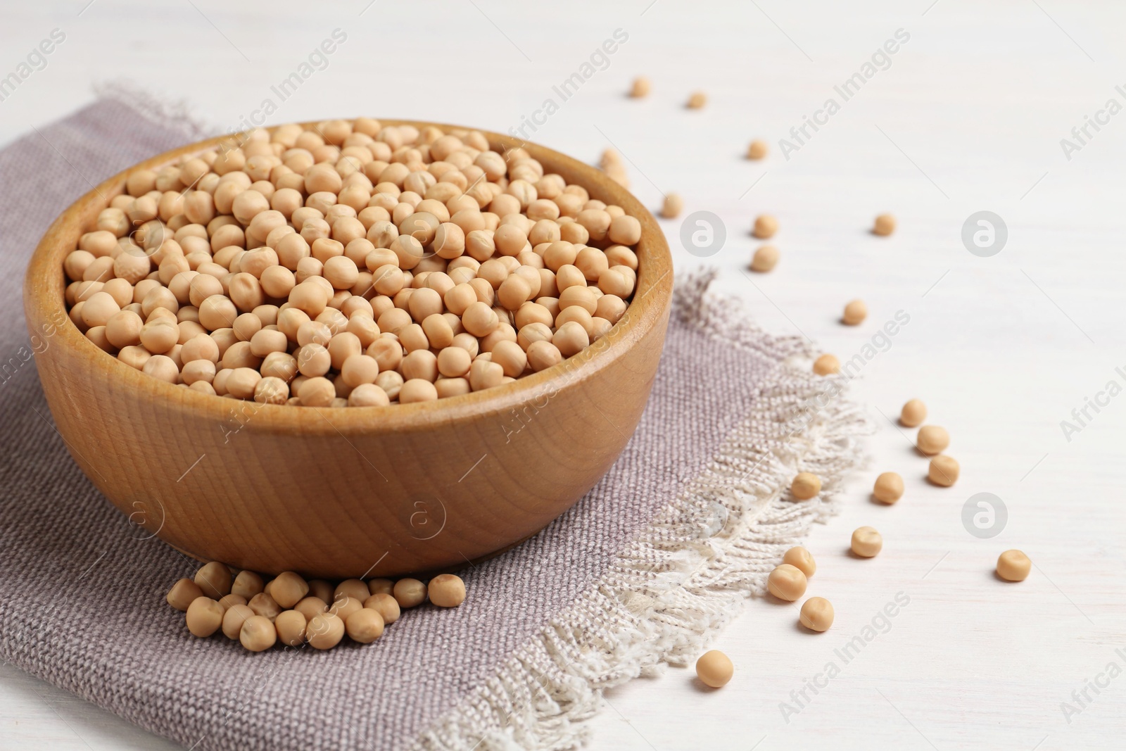 Photo of Dried peas in bowl on light wooden table, closeup