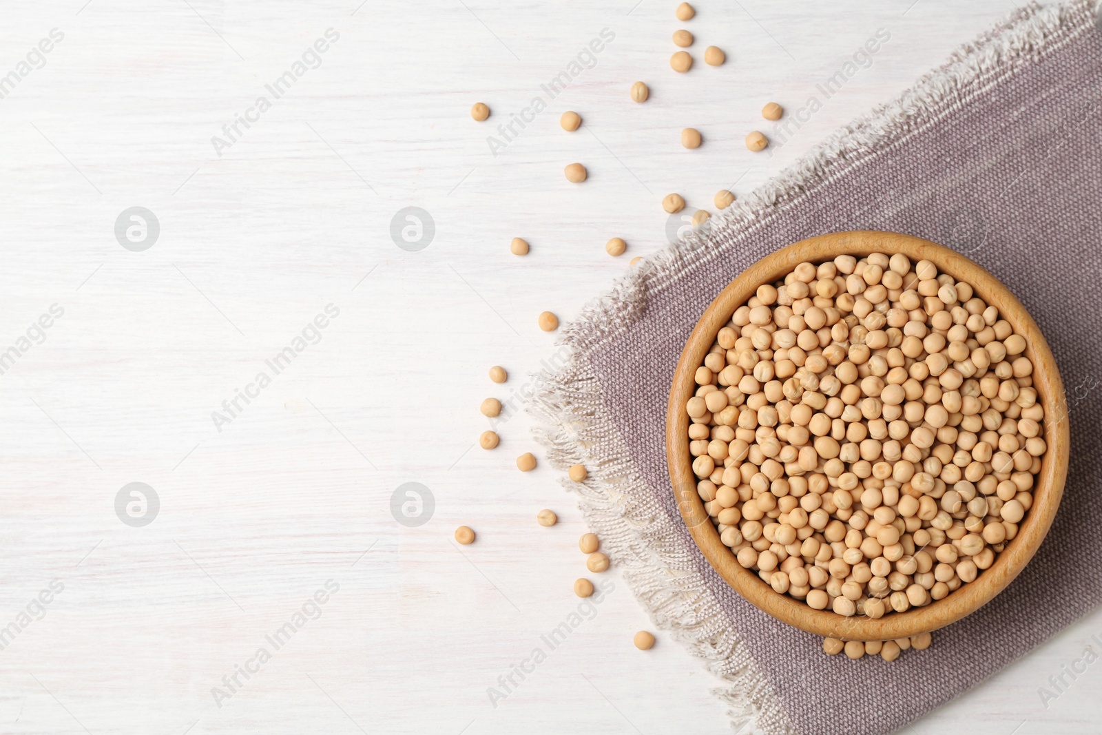 Photo of Dried peas in bowl on light wooden table, top view. Space for text