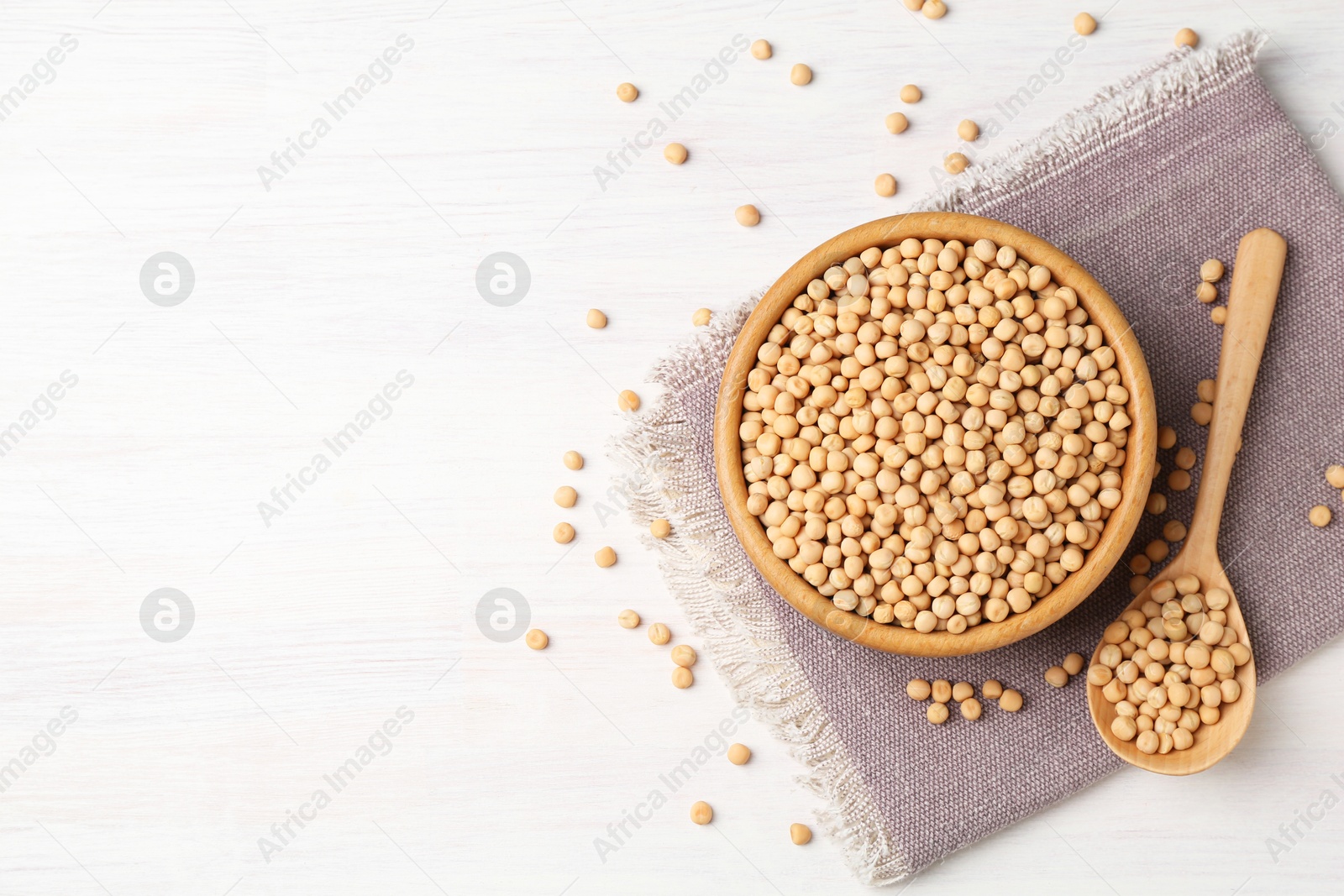 Photo of Dried peas in bowl and spoon on light wooden table, top view. Space for text