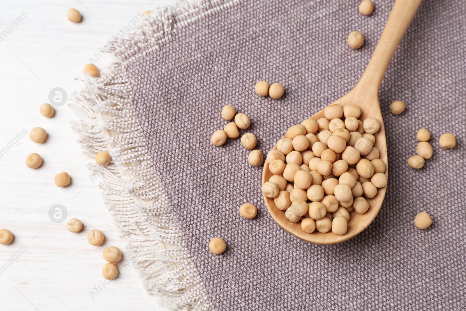 Photo of Spoon with dried peas on light wooden table, above view