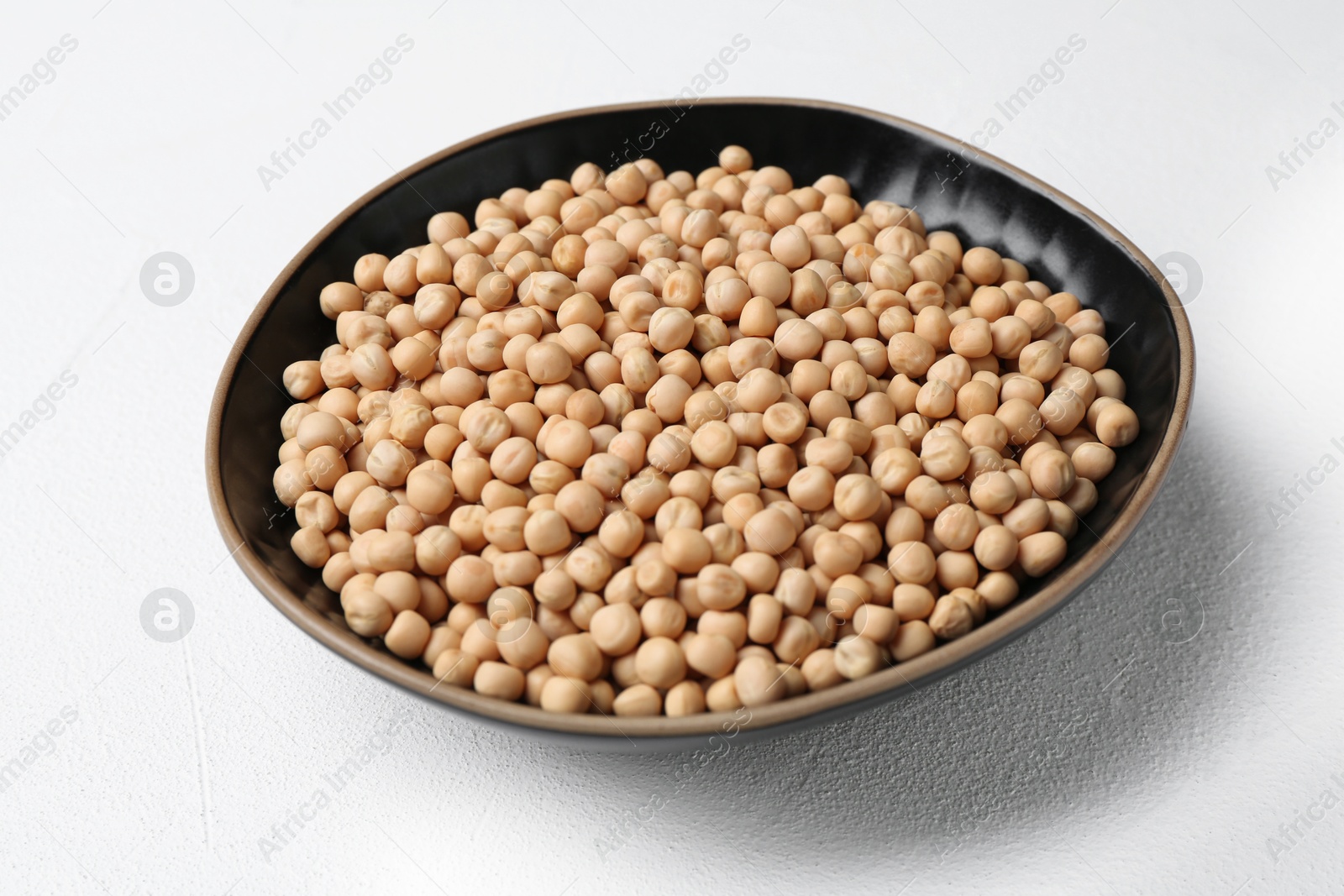 Photo of Dried peas in bowl on white textured table, closeup