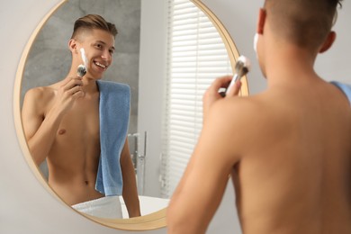 Handsome man applying shaving foam near mirror in bathroom