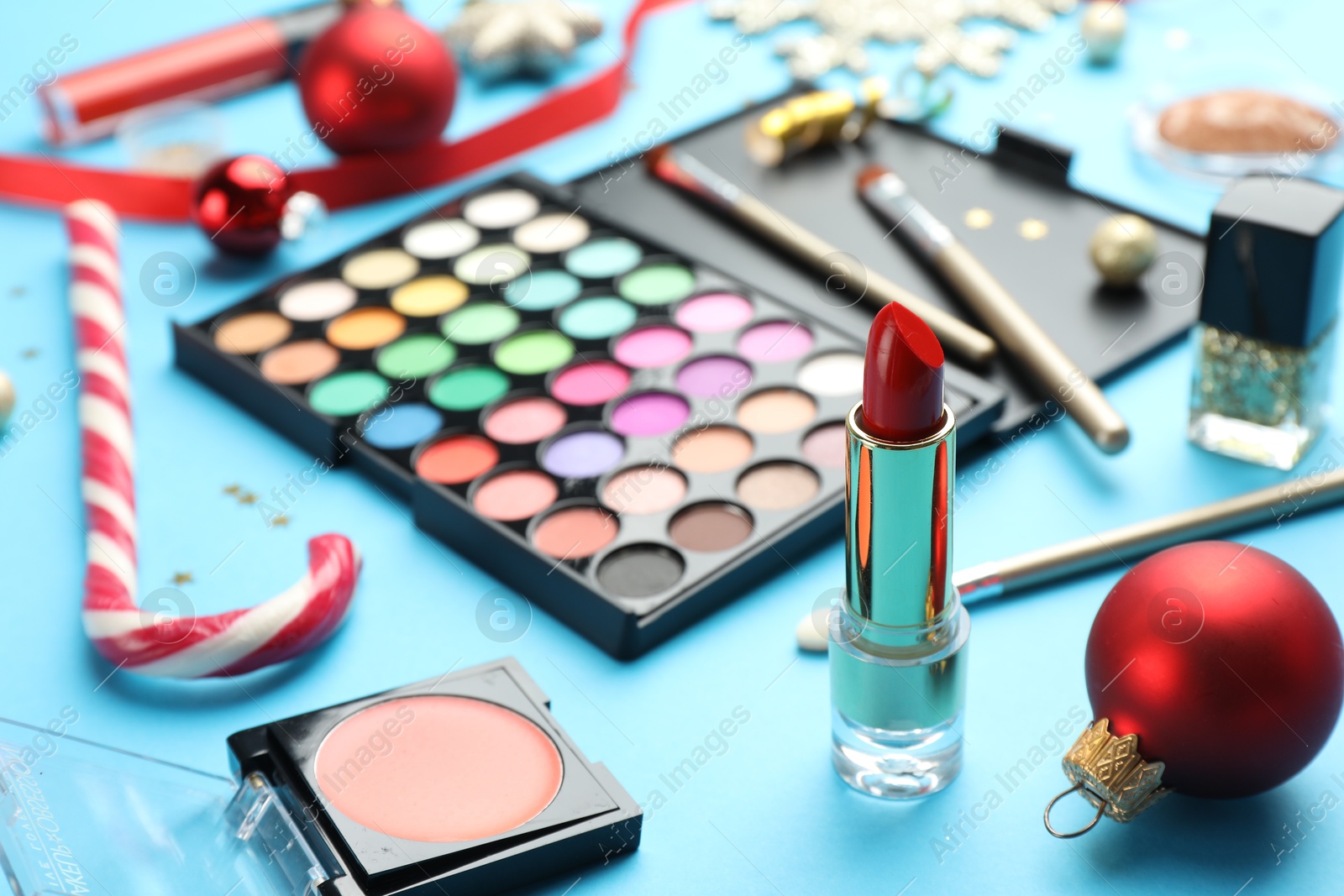 Photo of Different decorative cosmetic products and Christmas decor on light blue background, closeup