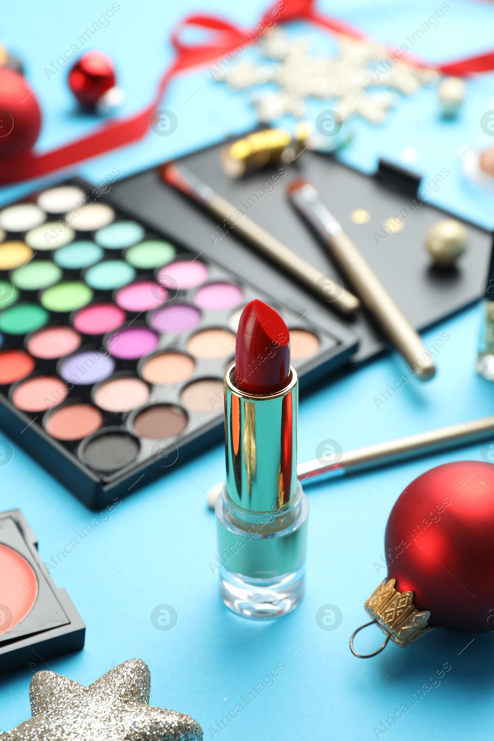 Photo of Different decorative cosmetic products and Christmas decor on light blue background, closeup