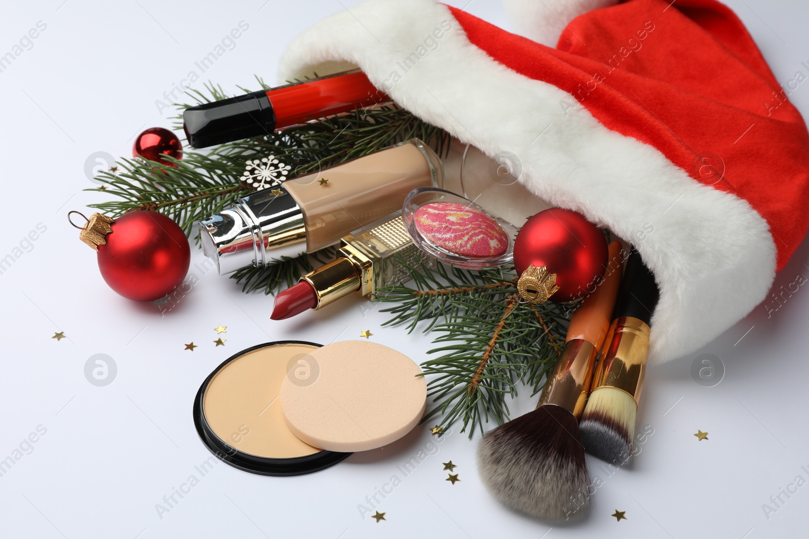 Photo of Santa hat with different decorative cosmetics and Christmas decor on white background, closeup