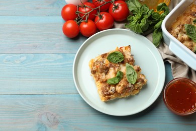 Photo of Tasty baked cauliflower, basil, tomatoes and sauce on light blue wooden table, top view. Space for text