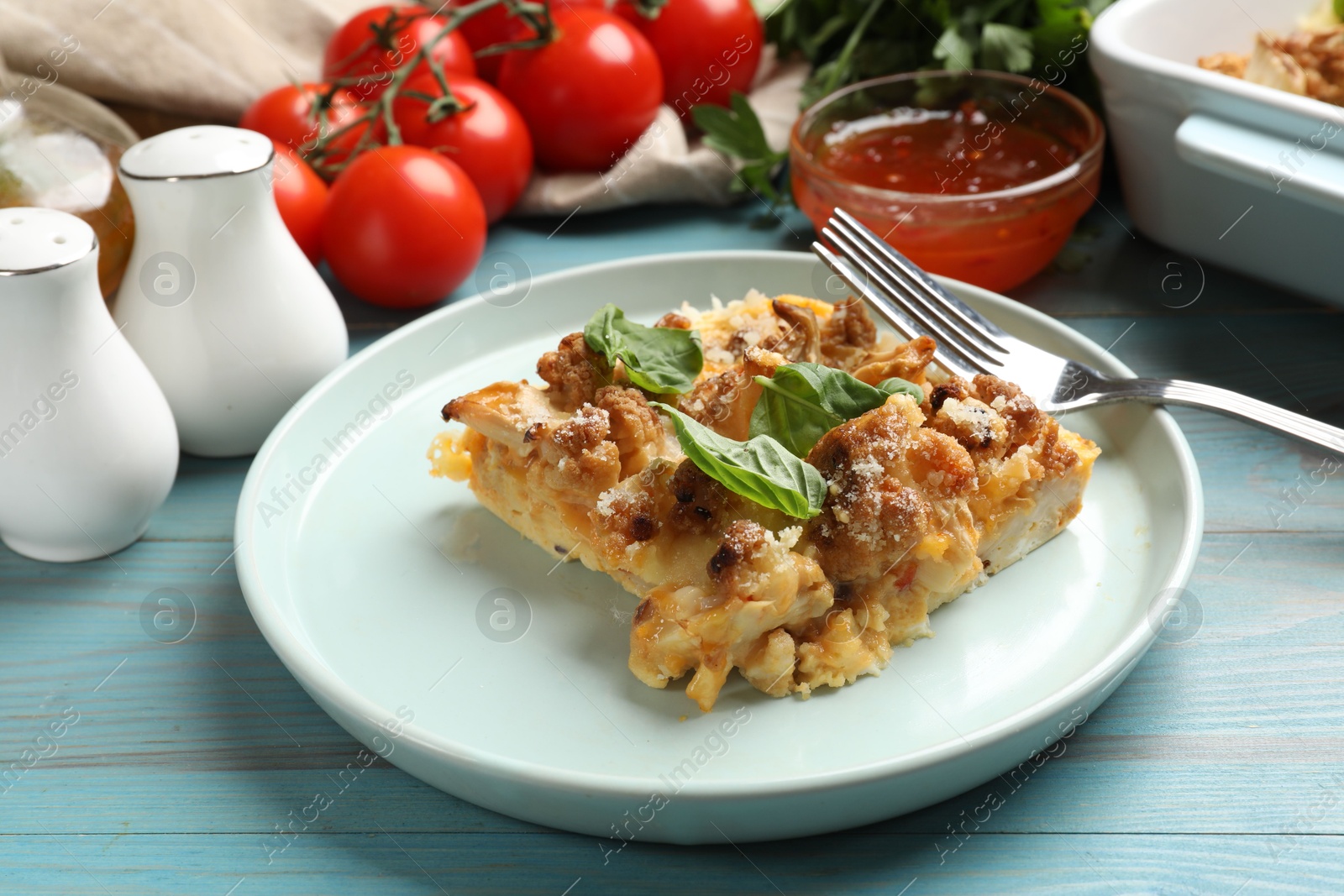 Photo of Tasty baked cauliflower, basil, spices, sauce and tomatoes on light blue wooden table, closeup