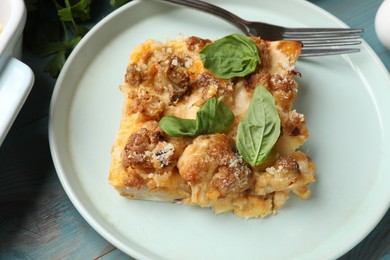 Tasty baked cauliflower and basil on light blue wooden table, closeup