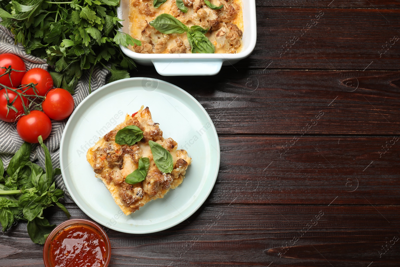 Photo of Tasty baked cauliflower, basil, parsley, sauce and tomatoes on wooden table, top view. Space for text