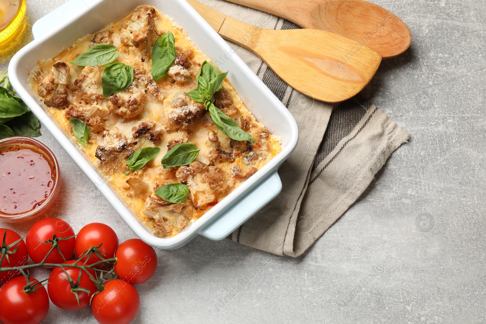 Photo of Tasty baked cauliflower in baking dish, basil, sauce and tomatoes on light grey table, top view