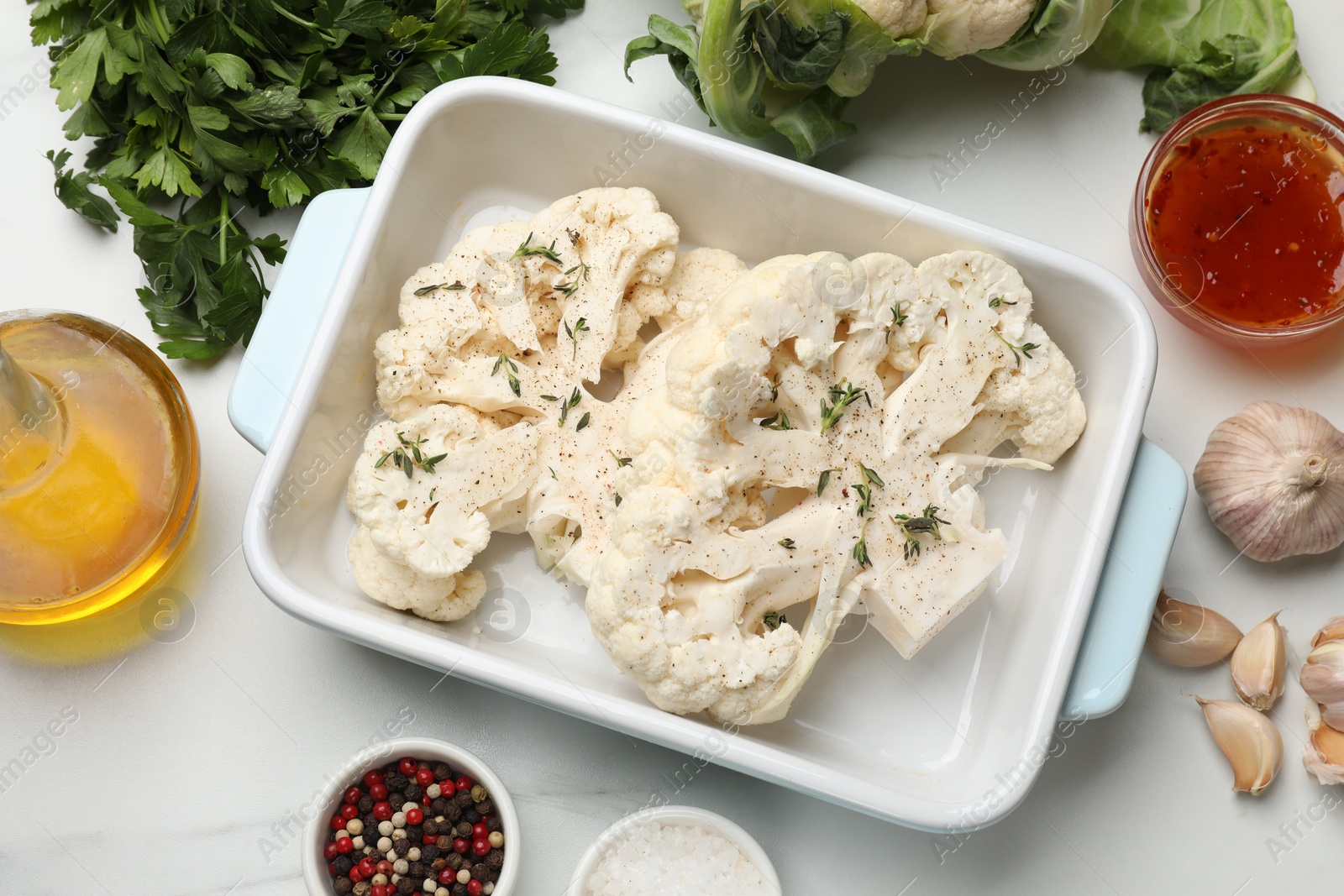 Photo of Uncooked cauliflower steaks, sauce, oil and spices on white marble table, flat lay