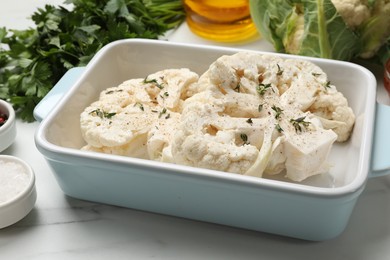 Photo of Uncooked cauliflower steaks and products on white marble table, closeup