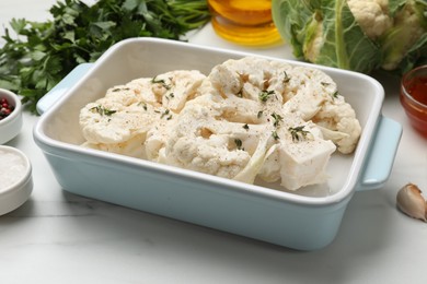 Photo of Uncooked cauliflower steaks and products on white marble table, closeup