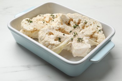 Photo of Uncooked cauliflower steaks with spices in baking dish on white marble table, closeup