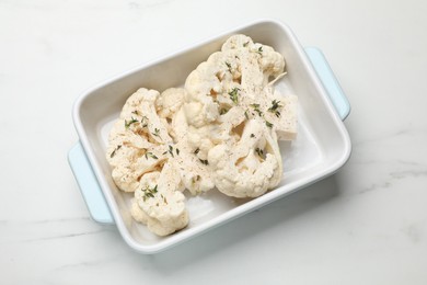 Photo of Uncooked cauliflower steaks with spices in baking dish on white marble table, top view