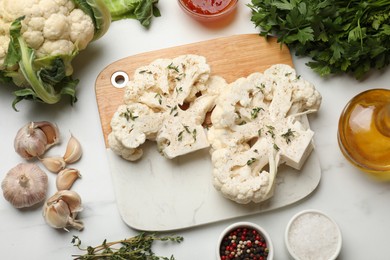 Photo of Uncooked cauliflower steaks, sauce, oil and spices on white marble table, flat lay