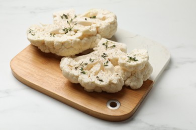 Photo of Uncooked cauliflower steaks with spices on white marble table, closeup