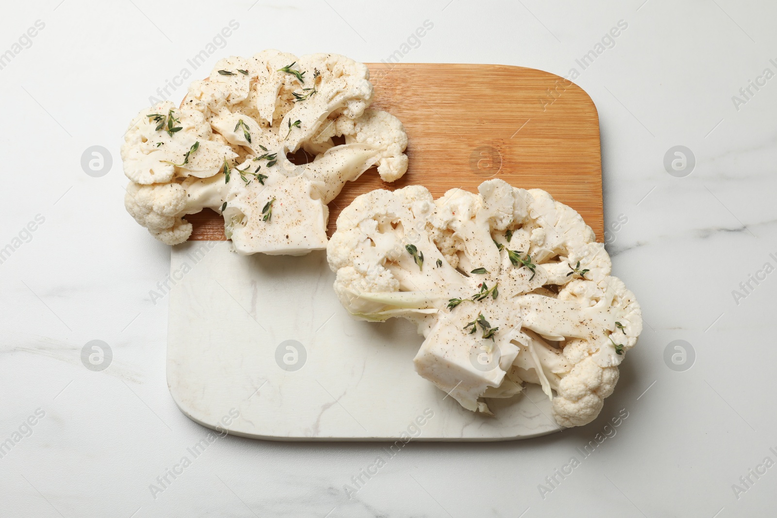 Photo of Uncooked cauliflower steaks with spices on white marble table, top view