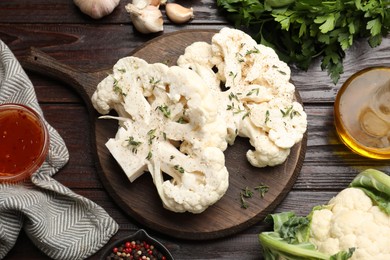 Photo of Uncooked cauliflower steaks, sauce, oil and spices on wooden table, flat lay