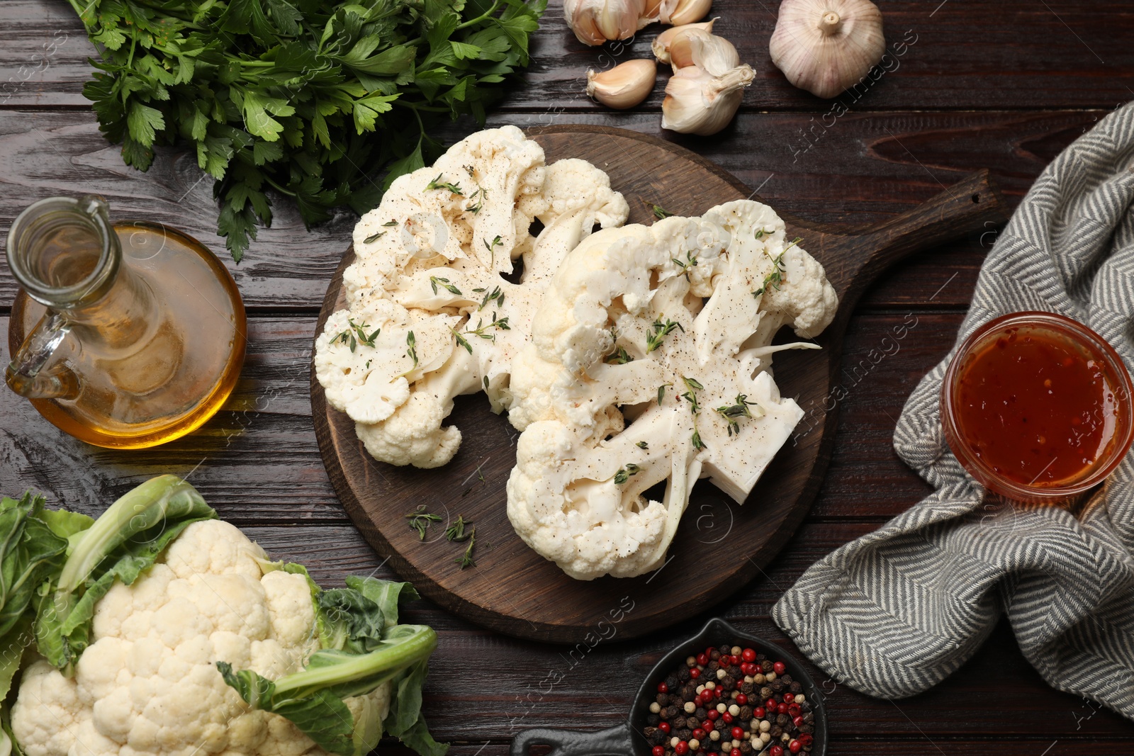 Photo of Uncooked cauliflower steaks, sauce, oil and spices on wooden table, flat lay