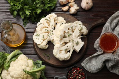 Photo of Uncooked cauliflower steaks, sauce, oil and spices on wooden table, flat lay