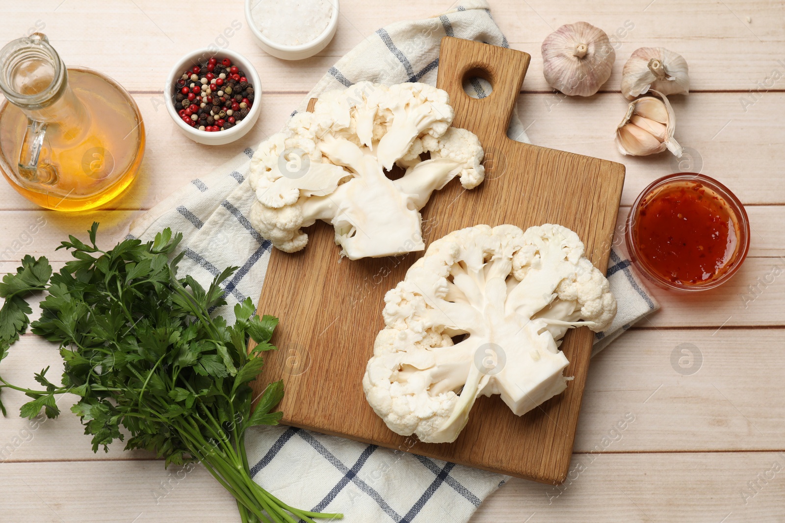 Photo of Uncooked cauliflower steaks, sauce, oil and spices on wooden table, flat lay