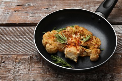 Photo of Tasty cauliflower steak and rosemary in frying pan on wooden table, closeup