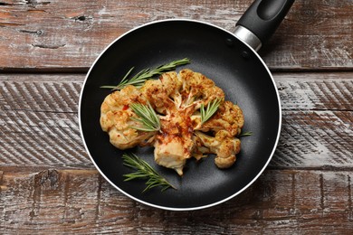 Photo of Tasty cauliflower steak and rosemary in frying pan on wooden table, top view