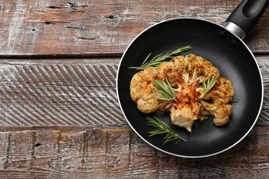 Photo of Tasty cauliflower steak and rosemary in frying pan on wooden table, top view. Space for text