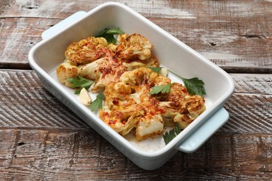 Photo of Tasty cauliflower steaks, parsley and garlic in baking dish on wooden table