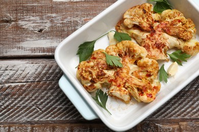 Photo of Tasty cauliflower steaks, parsley and garlic in baking dish on wooden table, top view