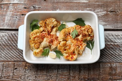 Photo of Tasty cauliflower steaks, parsley and garlic in baking dish on wooden table, top view